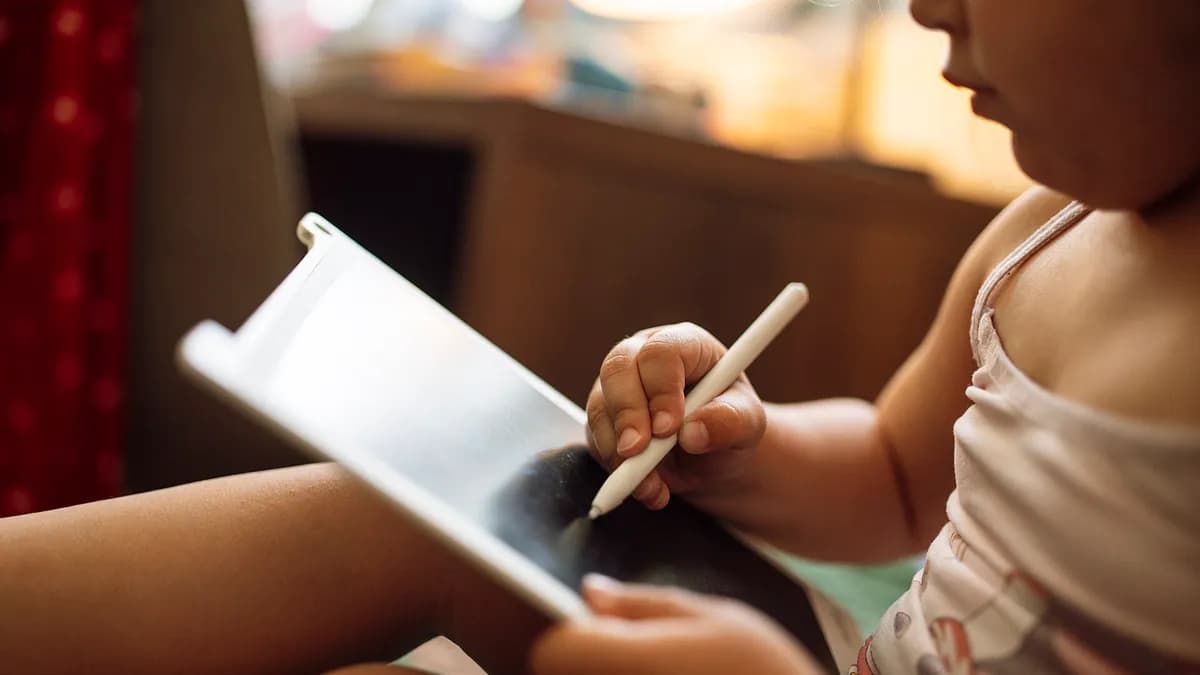 Dijete sjedi na krevetu i crta olovkom na tabletu
