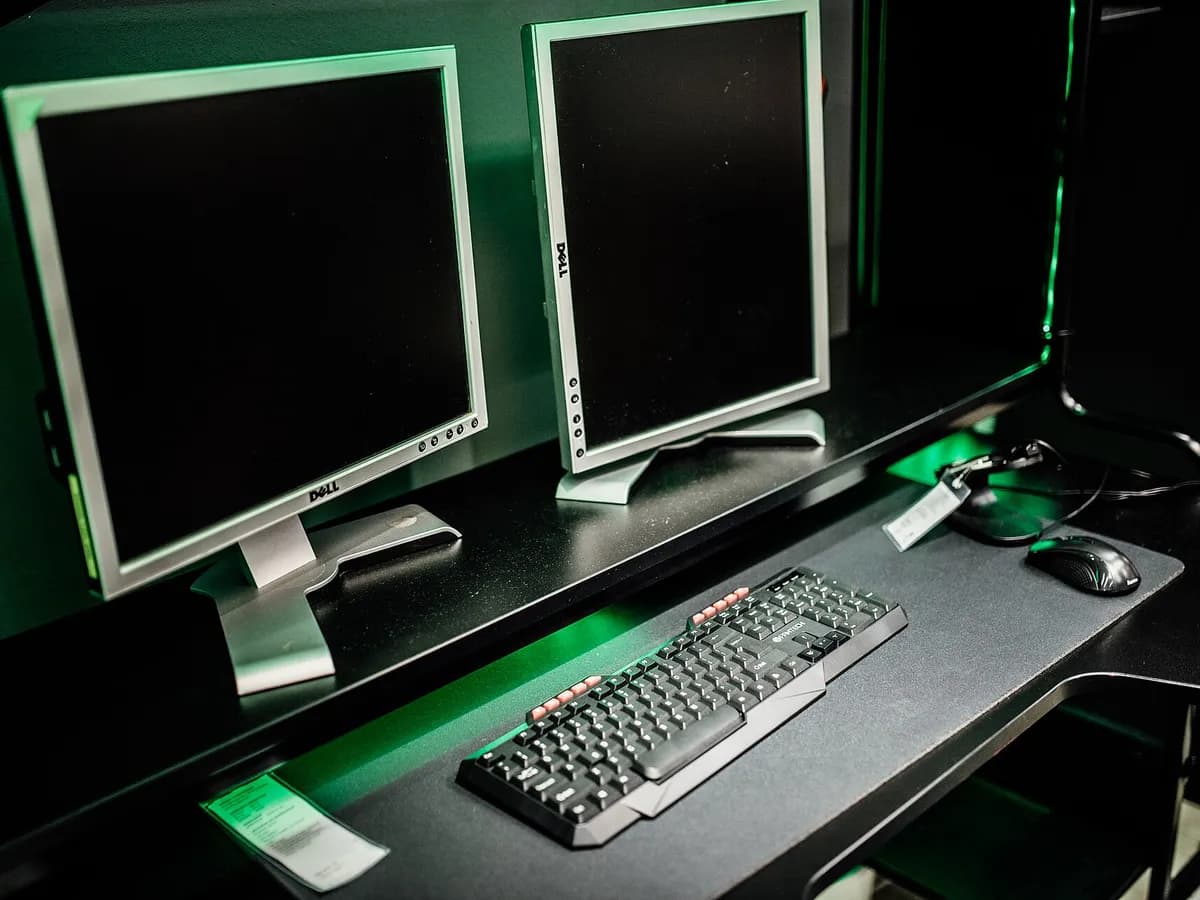 Ilustracija: dva monitora, tastatura i miš na stolu u sobi za igranje videoigara.
