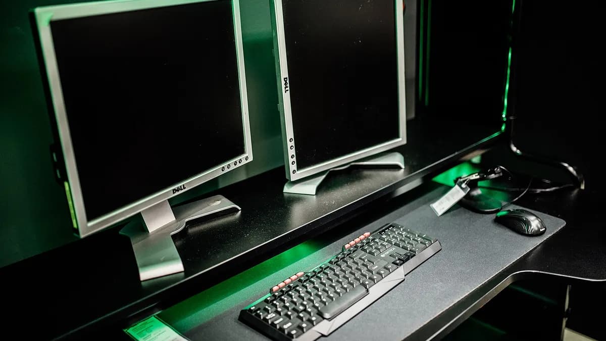 Ilustracija: dva monitora, tastatura i miš na stolu u sobi za igranje videoigara.